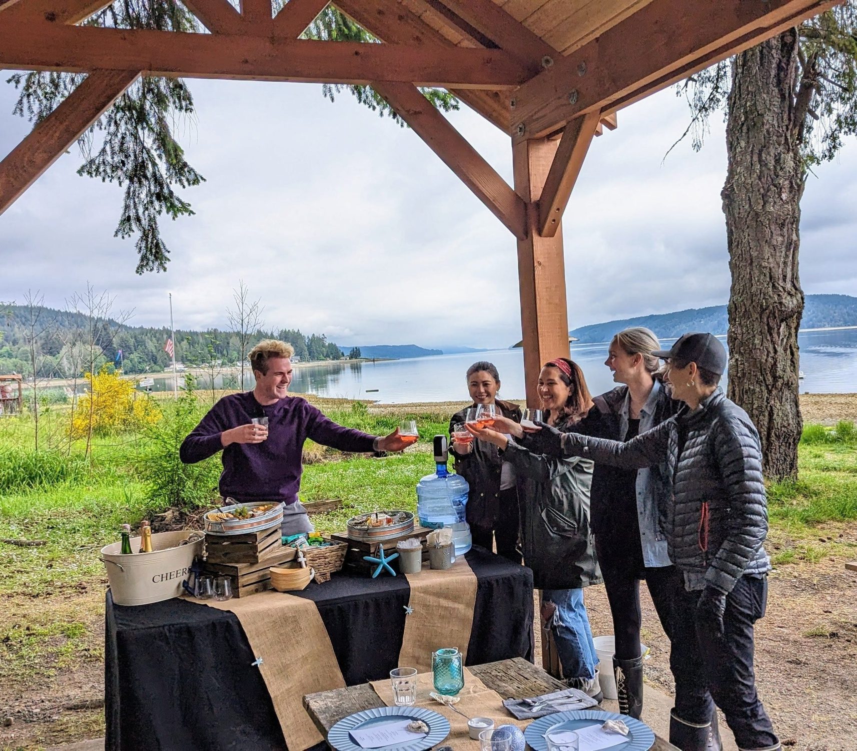 A group raises a toast at an outdoor table by the water
